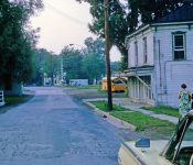 Village resident Helen Zubal (on right) and friend. The bus garage in the background which is now the post office . The railing on left is where the creek runs under 395 M-25