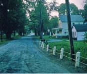 Looking towards the corner of East Shore Road and Main Street. The phone company and Methodist Church parsonage on right with a beautiful porch on the front of the building. M-31